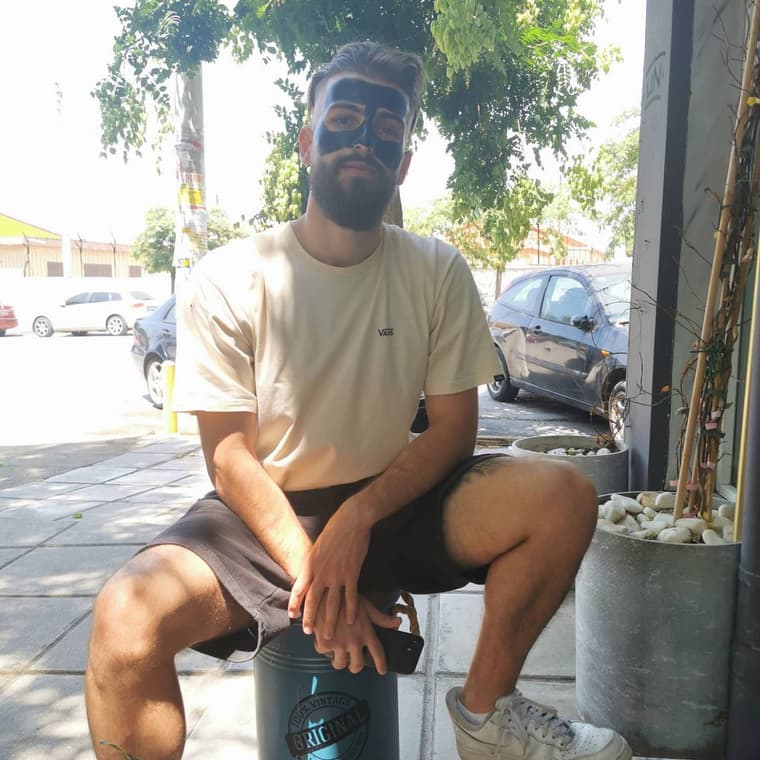 Πελάτης του LIORAS BARBERSHOP με μαύρη μάσκα άνθρακα, καθισμένος έξω στο πεζοδρόμιο μπροστά από το μαγαζί ένα καλοκαιρινό απόγευμα
